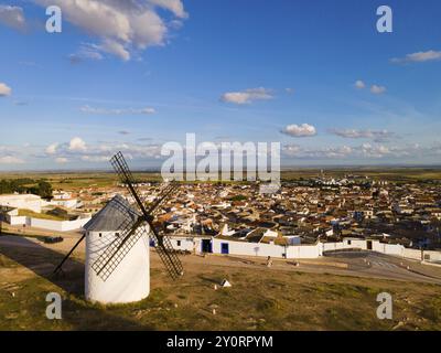 Windmühle mit Blick auf eine spanische Stadt, eingebettet in eine weite Landschaft unter einem klaren blauen Himmel mit ein paar Wolken, Luftblick, Windmühlen, Campo de Criptana, Stockfoto