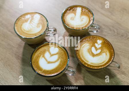 Vier Tassen Latte Art sitzen auf einem Holztisch und zeigen verschiedene Designs Stockfoto