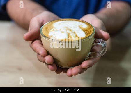 Hände eines jungen Barista, der Kaffee Latte Art macht, Inka Face Stockfoto