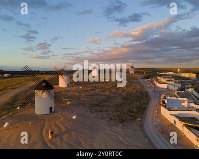 Landschaft bei Sonnenuntergang mit Windmühlen und einer Straße, die zu einem beleuchteten Dorf führt, Windmühlen aus der Luft, Campo de Criptana, Provinz Ciudad Real, Gegossen Stockfoto