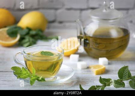 Eine Glasschale mit Tee, Pfefferminze und Zitrone, neben Zuckerwürfeln und einer Glaskanne auf einem Holztisch Stockfoto