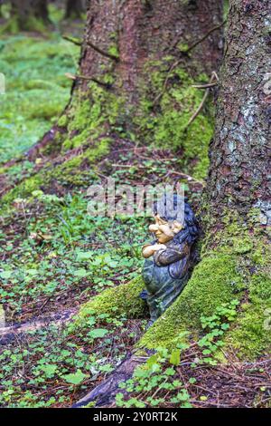 Troll lehnt sich an einen Baumstamm in einem Wald mit grünem Moos und Sauerampfer (Oxalis acetosella) Blätter Stockfoto