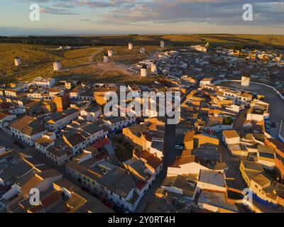 Dächer und Häuser eines Dorfes in der Abenddämmerung mit Windmühlen im Hintergrund und orangefarbener Beleuchtung, Luftaufnahme, Windmühlen, Campo de Criptana, Ciudad Real pro Stockfoto