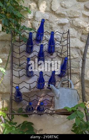 Ein Wandregal mit blauen Flaschen und einer alten Gießkanne vor einer Steinmauer. Pflanzen ragen von der Seite ins Bild, Oppede-le-Vieux, Vauc Stockfoto