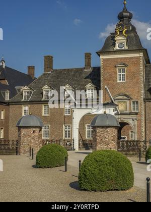 Haupteingang einer alten Burg mit Torbogen, Ziegelmauern, Türmen und gepflegten Hecken unter blauem Himmel, Anholt, Nordrhein-Westfalen, Deutschland, E Stockfoto