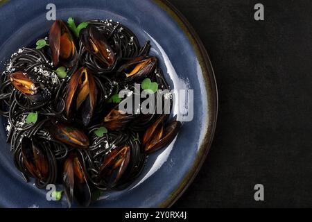 Spaghetti mit schwarzem Tintenfisch, schwarze Nudeln, mit gekochten Muscheln, auf einem schwarzen Teller, mit Petersilie und Parmesankäse, Nahaufnahme, selektiver Fokus, keine Leute Stockfoto