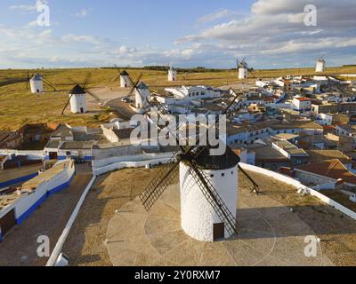 Viele Windmühlen in ländlicher Umgebung mit einem Dorf im Hintergrund unter bewölktem Himmel. Weiße Häuser und braune Dächer prägen die Landschaft. Antenne Stockfoto