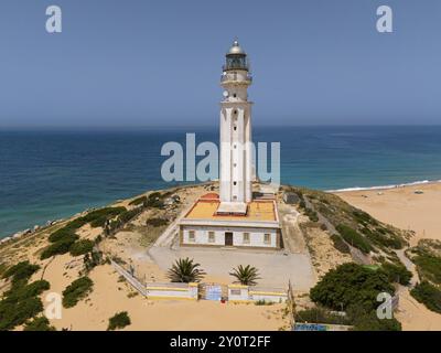 Weißer Leuchtturm an der Küste mit Blick auf das Meer und den Strand unter klarem Himmel, aus der Vogelperspektive, Faro de Trafalgar, Cape Trafalgar, Provinz Cadiz, Stockfoto