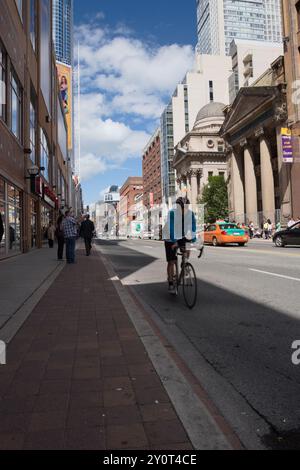 Eine belebte Straßenszene in Toronto mit Radfahrern, Fußgängern, historischen Gebäuden und modernen Wolkenkratzern unter hellem Himmel. Stockfoto