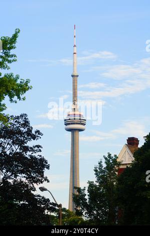 Ein Blick auf den CN Tower in Toronto, eingerahmt von grünen Bäumen und Wohndächern unter einem klaren blauen Himmel, der städtische und natürliche Elemente zeigt. Stockfoto