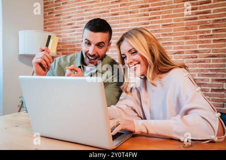 Ein junges kaukasisches Paar, das einen Laptop benutzt, um eine Online-Bestellung aufzugeben und mit seiner Kreditkarte dafür zu bezahlen. Zwei Leute, die online mit einem Computer einkaufen, sitzen im Wohnzimmer ihrer Wohnung. Hochwertige Fotos Stockfoto