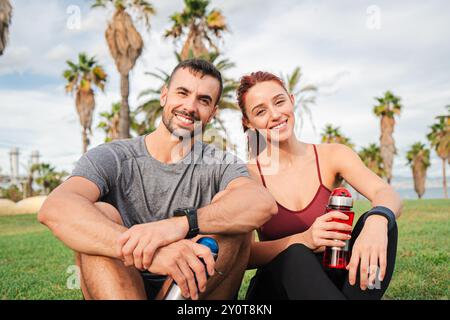 Ein fittes Paar, das nach einem Sprint mit Cardio-Workout auf dem Rasen sitzt, um seine Fitness zu verbessern. Zwei junge Leute, die nach einer intensiven Trainingsroutine in die Kamera schauen. Hochwertige Fotos Stockfoto