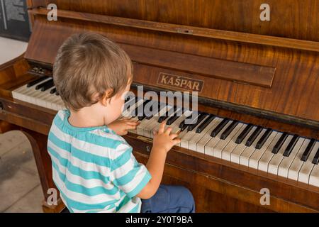 Ein kleiner Junge, der Klavier spielt, auf einem Stuhl sitzt, von hinten gesehen, drinnen Stockfoto