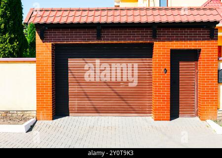 Garagentor unter einem rot gekachelten Dach mit klassischem Architekturstil und lebhaftem Farbkontrast. Garage mit einer Ziegelmauer und einem Bruder Stockfoto