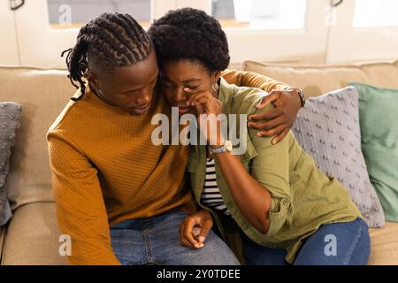 Tröstender Partner, afroamerikaner, der eine Frau auf der Couch zu Hause umarmt und tröstet Stockfoto