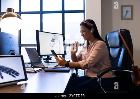 Videokonferenzen auf dem Smartphone, Frau winkt und lächelt im modernen Büro Stockfoto