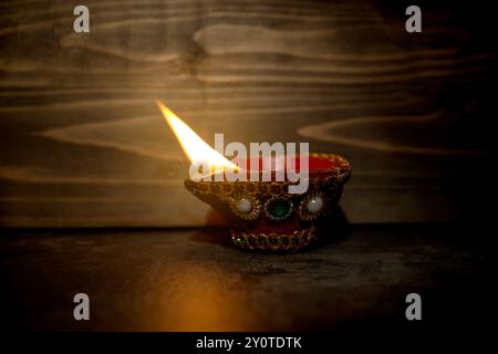 Ein rot-goldener Topf mit blauem und weißem Design steht auf einer dunklen Oberfläche. Im Topf brennt eine kleine Flamme. Diwali-Konzept Stockfoto