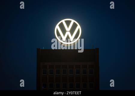 Wolfsburg, Deutschland. September 2024. Das VW-Logo glänzt am frühen Morgen auf dem Dach des Markenturms im Volkswagen Hauptwerk. Volkswagen hat angekündigt, seine Sparmaßnahmen aufgrund der angespannten Lage der Kernmarke zu verschärfen. Redundanzen und Werksschließungen können nicht mehr ausgeschlossen werden. Kredit: Moritz Frankenberg/dpa/Alamy Live News Stockfoto