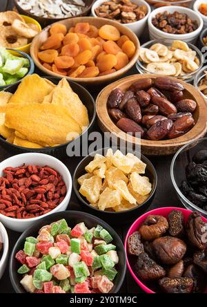 Mischung aus gesunden getrockneten süßen Früchten und Beeren in verschiedenen Schälchen auf schwarzem Hintergrund. Stockfoto