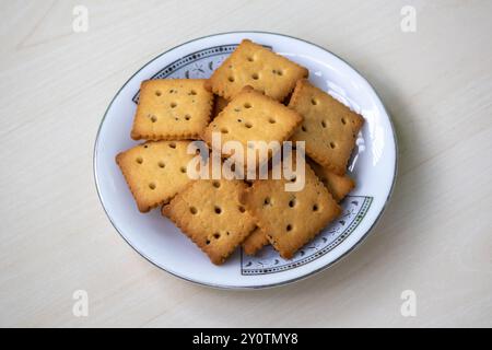 Köstliche Cracker-Kekse auf einem weißen Teller auf einer hellen Holzoberfläche. Kekse können jederzeit genossen werden, einschließlich Frühstück, Mittag- und Abendessen oder als Dinner Stockfoto