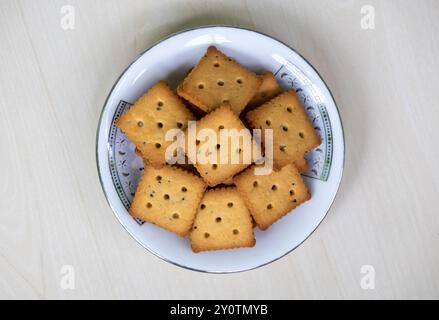 Knusprige Cracker-Kekse auf einer weißen Platte auf einer hellen Holzoberfläche. Kekse können jederzeit genossen werden, einschließlich Frühstück, Mittag- und Abendessen oder als Desse Stockfoto