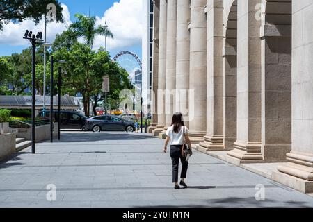 Hongkong, China - 03. Juli 2024 : Eine Frau läuft an einer Reihe von Säulen in einer Straße in Hongkong vorbei, Sonnenlicht scheint auf den Steinboden. Stockfoto