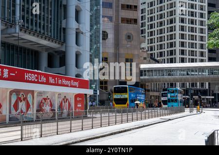 Hongkong, China - 03. Juli 2024 : Eine Stadtstraße in Hongkong, China, mit hohen modernen Gebäuden, einer Fußgängerbrücke und zwei Bussen, die auf der Th geparkt sind Stockfoto