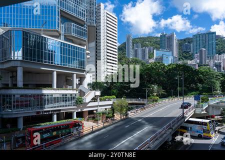 Hongkong, China - 03. Juli 2024 : urbane Szene in Hongkong mit einem Doppeldeckerbus, der am Straßenrand geparkt ist, einem Hügel, der von Grün bedeckt ist Stockfoto