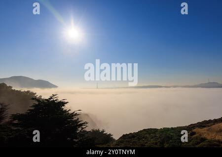 Helle Sonne und blauer Himmel über Nebel mit Golden Gate Bridge und Stadt in der Ferne Stockfoto