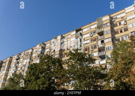 Ein großer typischer Apartmentblock im Stadtzentrum von Novi Sad in Serbien an einem sonnigen Sommertag mit blauem Himmel und Bäumen, mit Blick auf Fenster und Balkone. Stockfoto