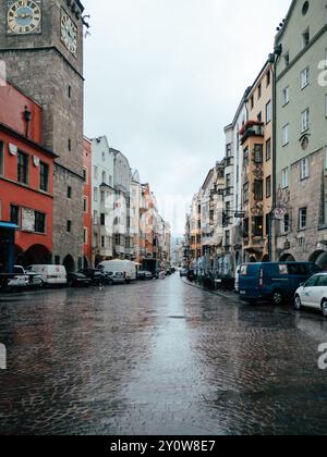 Eine nasse Kopfsteinpflasterstraße zieht sich durch die pulsierende Altstadt von Innsbruck und zeigt historische Gebäude unter grauem Himmel. Die Atmosphäre fühlt sich kal an Stockfoto