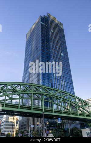 Der moderne Glasbüroturm erhebt sich über einer grünen Eisenbahnbrücke tokio japan Stockfoto