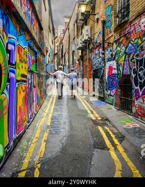 Zwei Personen laufen durch eine lebhafte, mit Graffiti bedeckte Gasse in Bristol Stockfoto