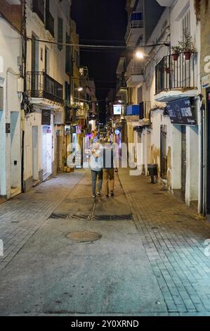 Sitges, Barcelona-04.September 2024: Lebendige Nacht in einer engen Fußgängerzone mit lokalem Charme und typischer Architektur. Stockfoto