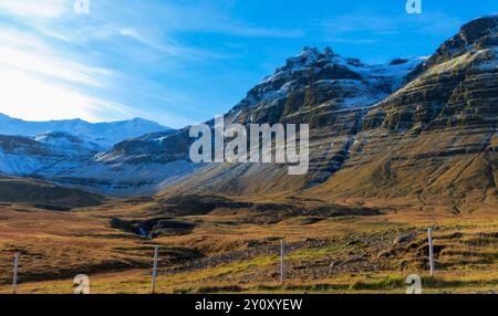 Eine Bergkette mit Schnee auf der Spitze und einem klaren blauen Himmel. Ein Holz- und Drahtzaun umgibt das Feld unter dem Berg Stockfoto