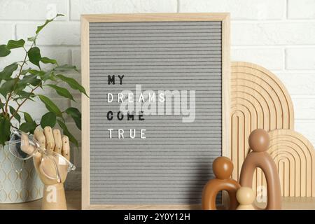Brieftafel mit dem Satz My Dreams Come True, Pflanzen- und Dekorationselemente auf Holztisch in der Nähe der weißen Ziegelwand Stockfoto