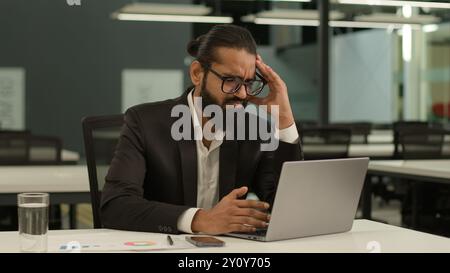 Gestresster kranker indischer männlicher Arbeitgeber Unternehmen arabischer Unternehmer Boss CEO Geschäftsmann muslimischer Geschäftsmann im Büro mit Laptop arbeitet Stockfoto