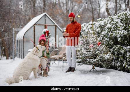 Junge Familie mit einem Hund im verschneiten Hinterhof während der Winterferien Stockfoto