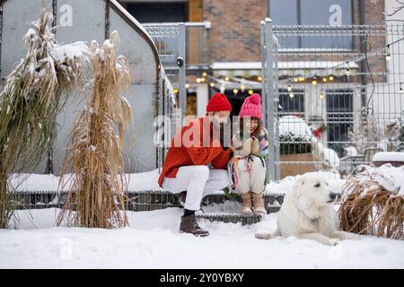 Ein junges Paar mit Hund auf der Veranda ihres Hauses im Winter Stockfoto