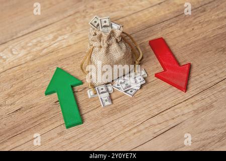 Ein Sack voller Dollarscheine zwischen einem grünen Aufwärtspfeil und einem roten Abwärtspfeil. Investitionsschwankungen, Marktvolatilität, Gewinn und Stockfoto