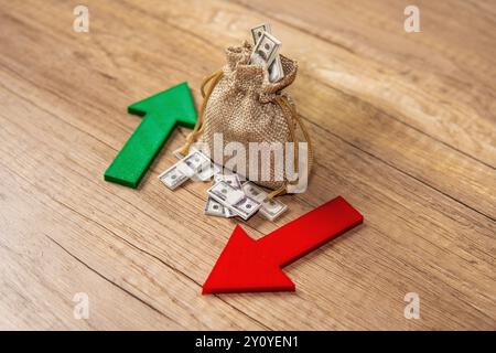 Ein Sack voller Dollarscheine zwischen einem grünen Aufwärtspfeil und einem roten Abwärtspfeil. Investitionsschwankungen, Marktvolatilität, Stockfoto