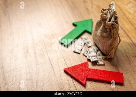 Ein Sack voller Dollarscheine zwischen einem grünen Aufwärtspfeil und einem roten Abwärtspfeil. Investitionsschwankungen, Marktvolatilität, Stockfoto