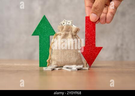 Ein Sack voller Dollarscheine zwischen einem grünen Aufwärtspfeil und einem roten Abwärtspfeil. Investitionsschwankungen, Marktvolatilität, Stockfoto