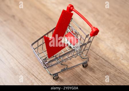 Ein Miniatur-Einkaufswagen mit nach unten zeigendem rotem Pfeil. Einzelhandelstrends, Umsatzrückgang, Konzept für Umsatzrückgang. Stockfoto