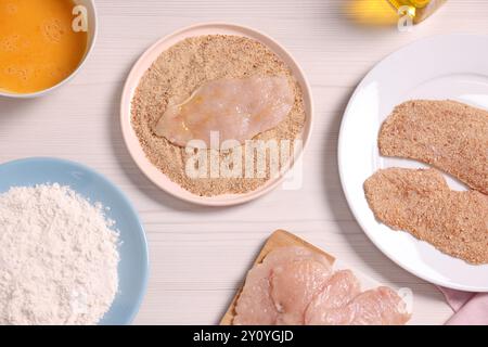 Schnitzel machen. Fleischscheiben mit Semmelbröseln und Zutaten auf weißem Holztisch, flach gelegt Stockfoto