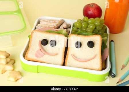 Sandwiches mit Smiley-Gesichtern in der Lunchbox, Flasche Saft, Bleistifte und Stift auf gelbem Tisch, Nahaufnahme Stockfoto