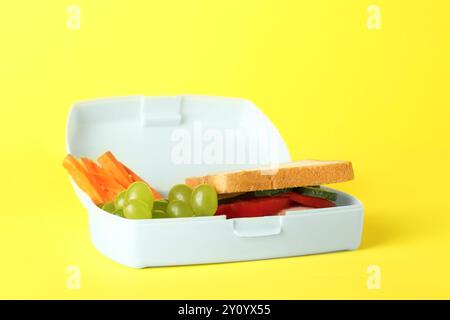 Lunchbox mit Sandwich, Karotte und Traube auf gelbem Hintergrund Stockfoto