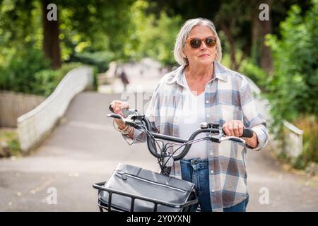 Ältere Frau, die im Park mit dem Elektrofahrrad fährt Stockfoto