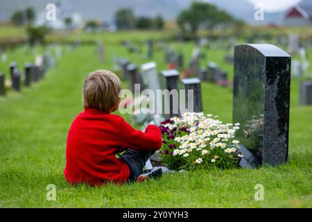 Trauriges kleines Kind, blonder Junge, im Regen auf dem Friedhof stehend, traurige Person, Trauer, Sommer regnerischer Tag Stockfoto