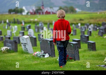 Trauriges kleines Kind, blonder Junge, im Regen auf dem Friedhof stehend, traurige Person, Trauer, Sommer regnerischer Tag Stockfoto